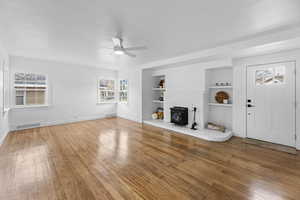 Living room with hardwood flooring, built in features, ceiling fan, and a wood stove