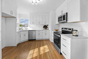 Kitchen featuring appliances with stainless steel finishes, white cabinetry, quartz countertops, and hardwood flooring