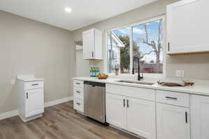 Kitchen with dishwasher, sink, white cabinets, and light hardwood / wood-style flooring