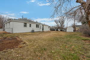 Rear view of property with a storage shed, a yard, and central AC unit