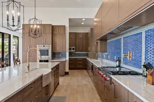 Kitchen featuring appliances with stainless steel finishes, decorative light fixtures, sink, light stone countertops, and custom range hood