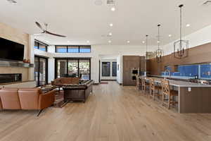 Living room featuring a towering ceiling, a large fireplace, ceiling fan, and light wood-type flooring