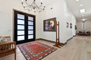 Entryway featuring a skylight, french doors, a chandelier, and light wood-type flooring