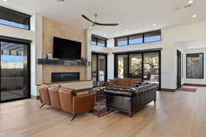 Living room with ceiling fan, a high ceiling, a tile fireplace, and light wood-type flooring