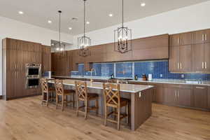 Kitchen with a breakfast bar, pendant lighting, a spacious island, a high ceiling, and light hardwood / wood-style flooring