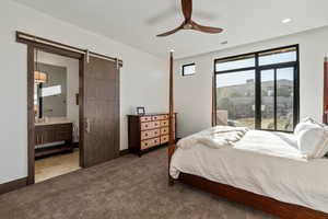 Carpeted bedroom featuring ensuite bath, a barn door, and ceiling fan