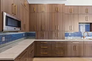 Kitchen with light stone counters, light hardwood / wood-style floors, sink, and decorative backsplash