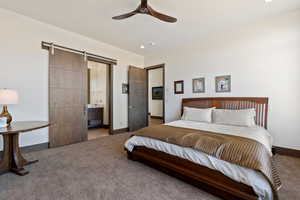 Carpeted bedroom with a barn door, ceiling fan, and ensuite bathroom