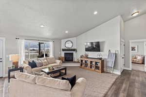 Living room with hardwood / wood-style floors, a fireplace, a textured ceiling, and vaulted ceiling