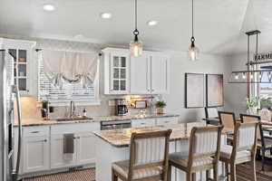 Kitchen with sink, white cabinetry, a center island, light stone counters, and decorative light fixtures