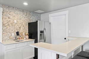 Kitchen featuring white cabinetry, kitchen peninsula, a kitchen breakfast bar, and stainless steel fridge with ice dispenser