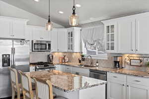 Kitchen with decorative light fixtures, stainless steel appliances, white cabinets, and a kitchen island