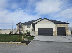 View of front facade with a garage, concrete driveway, stone siding, and a front lawn