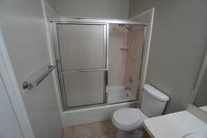 Full bathroom featuring toilet, vanity, shower / bath combination with glass door, and tile patterned flooring