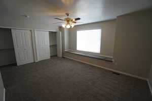 Unfurnished bedroom with multiple closets, ceiling fan, and dark carpet