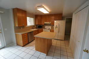 Kitchen with sink, tasteful backsplash, light tile patterned floors, appliances with stainless steel finishes, and a kitchen island