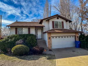 Tri-level home with brick siding, driveway, a garage, and roof with shingles