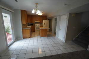 Kitchen featuring light tile patterned flooring, white appliances, decorative light fixtures, and a center island