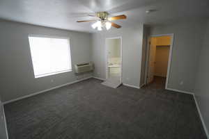 Unfurnished bedroom featuring a spacious closet, an AC wall unit, a textured ceiling, and dark colored carpet