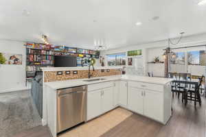 Kitchen with hardwood / wood-style floors, sink, white cabinets, stainless steel dishwasher, and kitchen peninsula