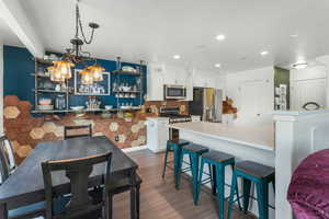 Kitchen featuring dark wood-type flooring, a breakfast bar, appliances with stainless steel finishes, pendant lighting, and white cabinets