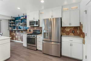 Kitchen featuring decorative backsplash, appliances with stainless steel finishes, white cabinets, and light hardwood / wood-style flooring