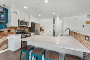 Kitchen featuring white cabinetry, sink, a breakfast bar area, kitchen peninsula, and stainless steel appliances