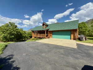 Cabin featuring log exterior, covered porch, asphalt driveway, a mountain view, and a garage