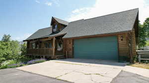 Log cabin featuring a porch, a shingled roof, log siding, an attached garage, and concrete driveway