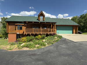 Cabin with brand new roof, log siding, driveway, a 2-car garage, and covered porch