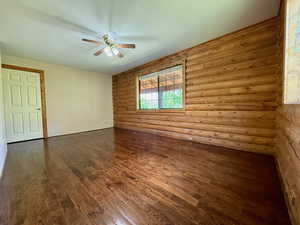 Main floor bedroom featuring a ceiling fan, hardwood flooring and log walls