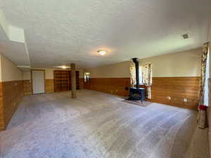 Large family room featuring wooden walls, wainscoting, a textured ceiling, a wood stove, and carpet flooring