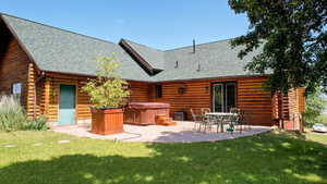 Rear view of house with a hot tub, log exterior, a patio, and a shingled roof
