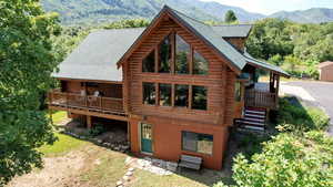 Rear view of house featuring log exterior, a deck with mountain view, and a shingled roof