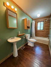 Main floor hall bathroom with toilet, baseboards, shower / tub combo, wood finished floors, and log walls