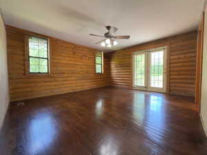 Mater bedroom with ceiling fan, dark wood finished floors, lots of natural light and log walls
