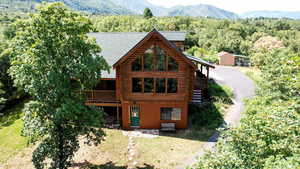 View of front of house with log siding, a forest view, a shingled roof, and a deck with mountain view