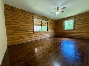 Main floor bedroom featuring log walls, hardwood flooring, and a ceiling fan