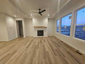 Unfurnished living room with a raised ceiling, ceiling fan, and light wood-type flooring