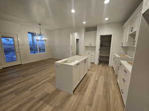 Kitchen featuring a notable chandelier, a kitchen island, white cabinets, and light hardwood / wood-style floors