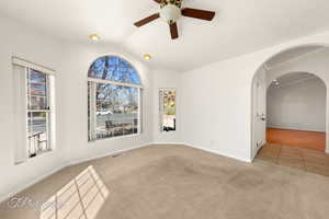 Empty room featuring ceiling fan, light colored carpet, and lofted ceiling