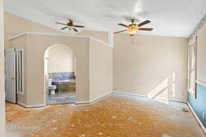 Unfurnished room featuring ceiling fan, vaulted ceiling, and a textured ceiling