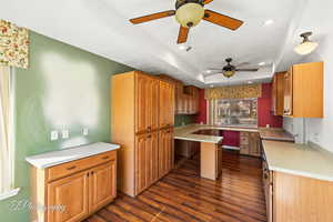 Kitchen with built in desk, ceiling fan, a raised ceiling, dark wood-type flooring, and a textured ceiling