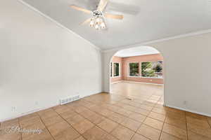 Unfurnished room with vaulted ceiling, light tile patterned floors, ceiling fan, crown molding, and a textured ceiling