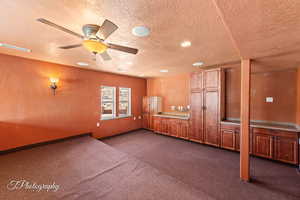 Unfurnished room featuring dark colored carpet, ceiling fan, and a textured ceiling