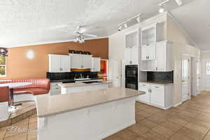 Kitchen featuring white cabinetry, vaulted ceiling, black appliances, and a center island