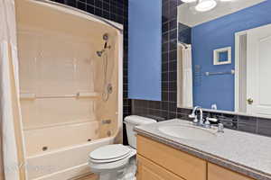 Full bathroom featuring vanity, tile walls, shower / bath combination with curtain, and toilet