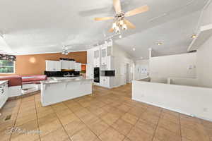 Kitchen with vaulted ceiling, a kitchen island, white cabinetry, a kitchen bar, and a textured ceiling