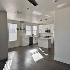 Kitchen with pendant lighting, white cabinetry, stainless steel appliances, and a kitchen island