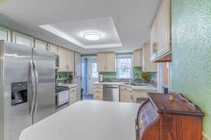 Kitchen with sink, stainless steel appliances, cream cabinets, a textured ceiling, and a raised ceiling